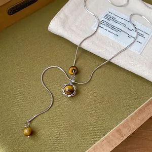 Détail d'un collier minimaliste avec perles œil de tigre et pendentif hexagramme argenté.