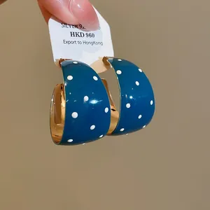 Detailopname van blauwgroene C-vormige oorbellen met witte stippen en gouden binnenkant.