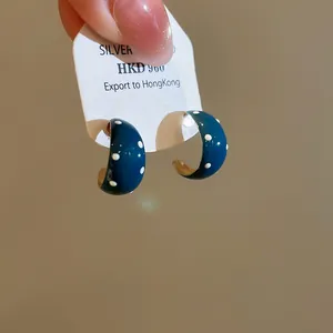 Detail van retro blauwe emaille C-vormige oorringen met witte polkadots print