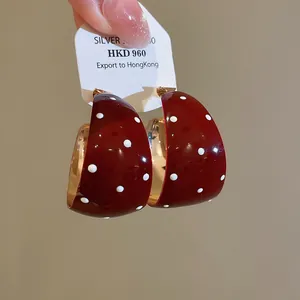 Detail van retro bordeauxrode C-vormige oorbellen met witte stippen en lakafwerking