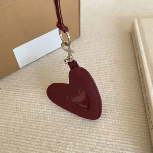 Gros plan d'un pendentif en cuir en forme de cœur bordeaux sur un fond beige texturé