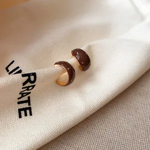 Detailweergave van bruine emaille C-vormige oorringen met witte stippen op een stoffen zak.