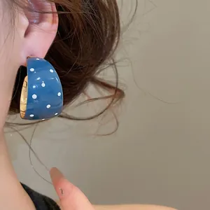 Detailopname van blauwe C-vormige oorringen met witte stippen op een model