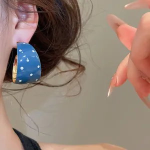 Detailopname van de blauwe C-vormige emaille oorbel met witte polkadots in retrostijl