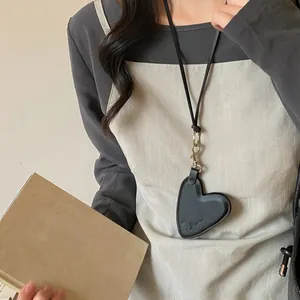 Détail d'une pochette de cou en cuir noir en forme de cœur avec un élégant fermoir doré.
