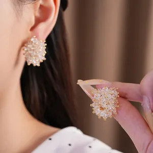 Close-up of sparkling glass bead cluster earrings worn on ear and held in hand