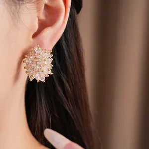 Close-up view of elegant clear glass cluster stud earrings with gold accents worn on an ear