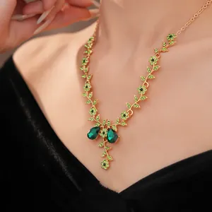 Primo piano di una collana vintage dorata con dettagli di fiori e foglie verdi.