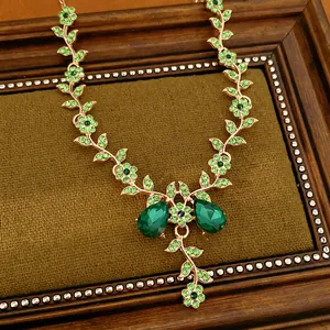 Dettaglio della collana vintage dorata con strass verdi a forma di fiore e foglia