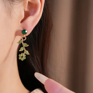 Dettaglio di orecchini vintage dorati con strass verdi a forma di fiore e foglia