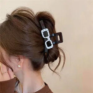 Detailed view of a unique acrylic sunglasses-shaped hair claw clip worn on brown hair.