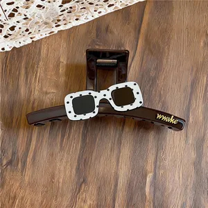Close-up of stylish acrylic hair claw clip with black and white polka dot sunglasses design