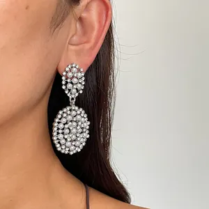 Détail rapproché de boucles d'oreilles ovales argentées avec perles et strass.