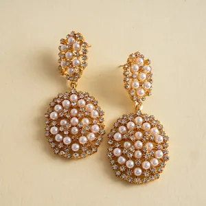 Vue détaillée de boucles d'oreilles ovales dorées ornées de perles et de strass étincelants.