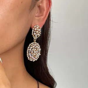 Gros plan de boucles d'oreilles pendantes ovales dorées avec perles et cristaux sur un mannequin