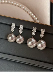 Detailed close-up showing two pairs of elegant pearl drop earrings with zircon crystals