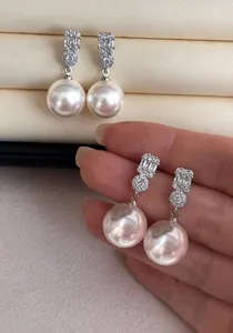 Close-up detail of elegant white pearl drop earrings with sparkling crystals held in hand.