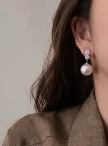 Elegant French style pearl drop earrings with sparkling zircon inlay shown on ear.
