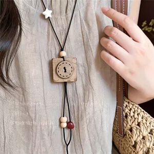 Close-up of a vintage-style wooden square pendant necklace on a beige textured garment.
