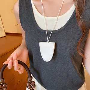 Detail van een witte leren brillenhouder hanger aan een minimalistische ketting