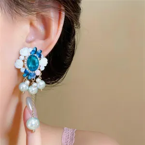 Nahaufnahme von blauen Edelstein-Ohrringen mit eleganten Perlen am Ohr des Models