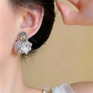 Elegantes pendientes plateados con cristal ovalado y diseño de hoja en la oreja del modelo