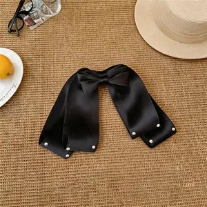 Barrette à cheveux avec nœud en satin noir et perles sur fond de natte de paille