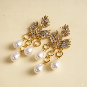 Gedetailleerde macro-opname van elegante gouden blad oorbellen met strass en parels.