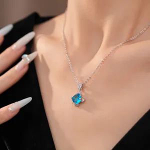 Nahaufnahme einer eleganten Silberkette mit blauem Zirkon-Anhänger am Hals einer Frau.