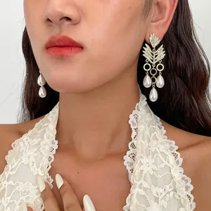 Detailweergave van elegante bladvormige strass oorbellen met parels gedragen door een model.