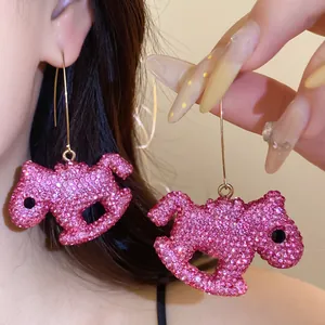 Close-up detail of sparkling pink rhinestone rocking horse dangle earrings on a model.