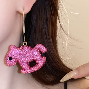 Close-up of a pink rhinestone-studded clay animal pendant earring shown on a model.
