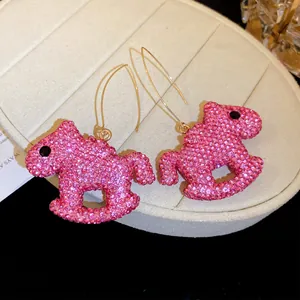 Close-up detail of pink rocking horse ear hook earrings with shimmering pink crystals.