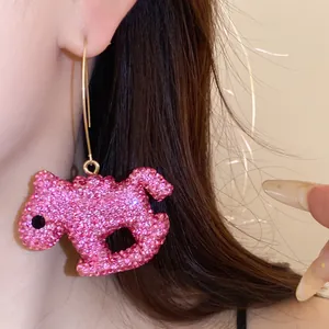 Detail view of sparkly pink rocking horse earring with gold hook worn on ear.