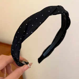 Detail eines schwarzen, gedrehten Stoff-Stirnbands mit eleganten weißen Punkten.