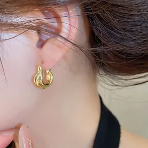 Detailaufnahme goldener C-förmiger Creolen mit eleganter unregelmäßiger Wellenstruktur