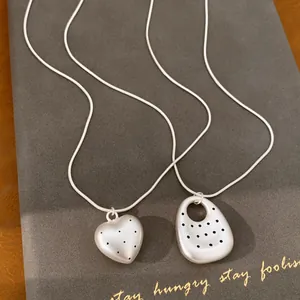 Macro detail of matte sand silver heart and oval pendants with polka dot pattern