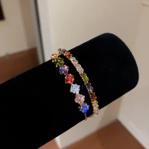 Close-up of 18k gold plated open bangle with colorful square zircons on black display.