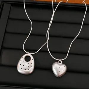 Close-up of matte silver necklaces with heart and oval pendants on a black tray.