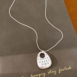Detail macro view of matte silver spotted oval pendant necklace with minimalist design