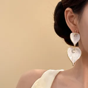 Elegante weiße Emaille-Ohrringe in Herzform am Ohr eines Modells in Nahaufnahme