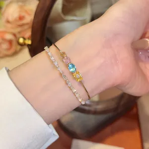 Close-up of 18k gold plated bangle with colored stones and a sparkling zircon bracelet
