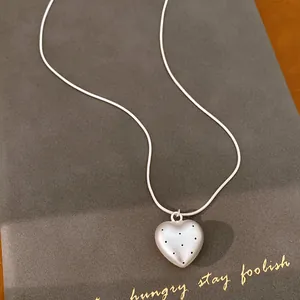 Close-up detail of sand silver heart pendant necklace featuring black star spot patterns