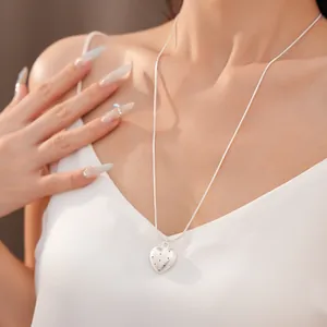 Detail of minimalist silver heart necklace with star spot texture on snake chain