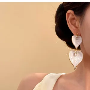 Detailansicht eleganter weißer Emaille-Herzohrringe, getragen am Ohr eines Models