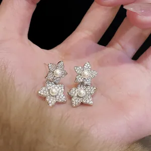 Close-up of floral stud earrings with micro-set zircons and pearls on silver needles.