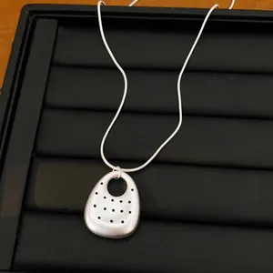 Detail view of matte silver oval pendant necklace with dotted pattern on black tray