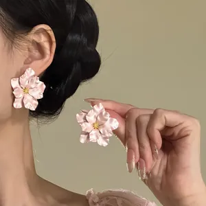 Detailansicht eleganter rosa Blumenohrstecker an Ohr und Hand eines Models gezeigt.