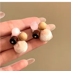 Close-up of pink cat-eye stone and wooden bead earrings with soft fabric pom-poms.