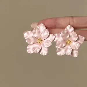 Nahaufnahme von eleganten rosa Blumen-Ohrsteckern mit goldenen Staubblättern auf Fingern.